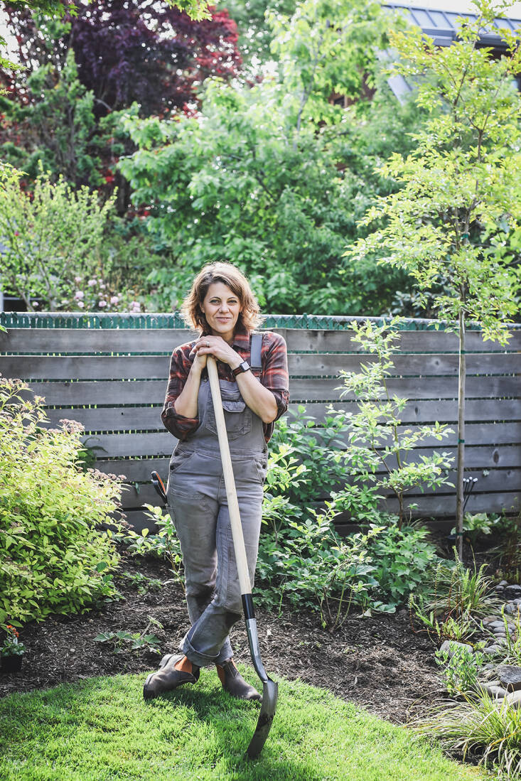 Kate is wearing Dovetail&#8217;s Freshley Overalls in gray canvas. Her muddy wet knees signaling a productive gardening day.