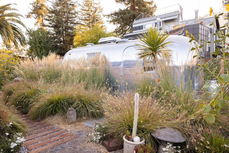 Stephanie and Lawrence remodeled a \1966 Airstream so that friends and family can stay here during visits. It also serves as the property’s restroom, as there is no other bathroom on the property. Upright Karl Foerster feather reed grass and red bunny tails fountain grass soften the Airstream and pathway.