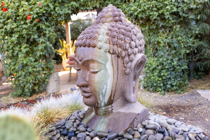 A generously-sized Buddha head that the couple uses as a water feature. Red passion flowers bloom in the background.